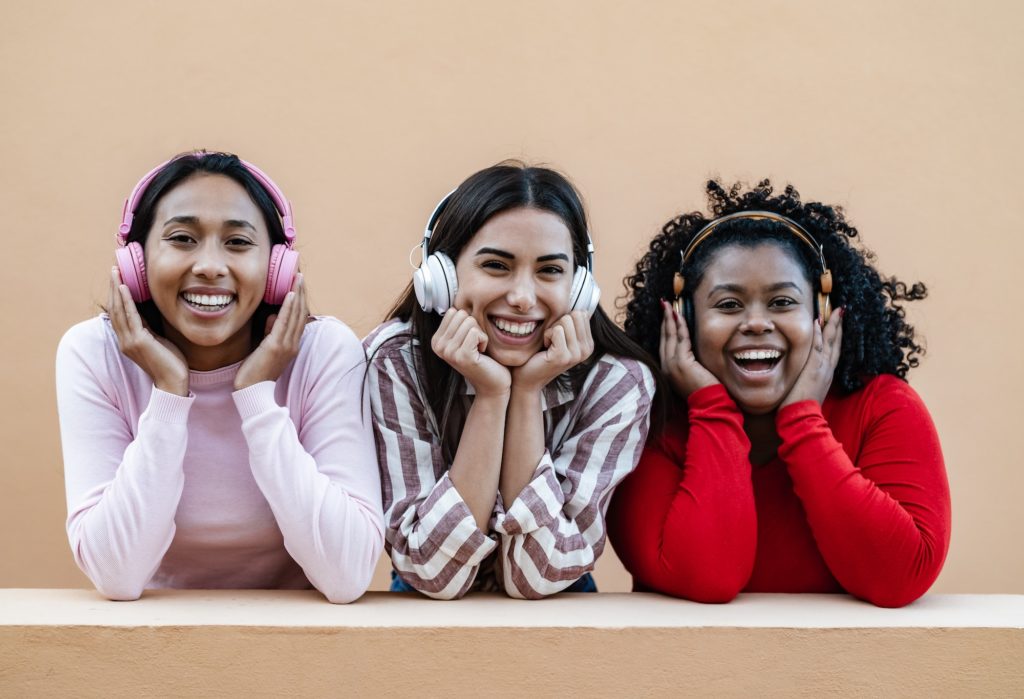 Three young ladies actively listening to music through their headphones.